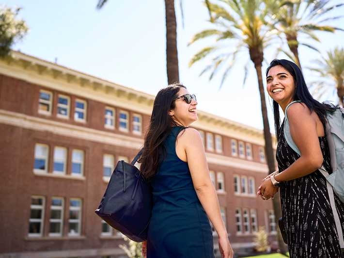 Two students posing in front of palm trees